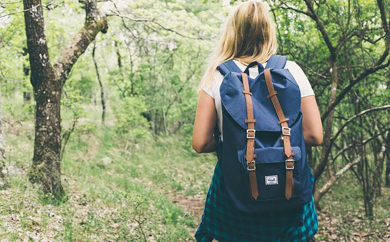teen girl walking in woods with a backpack on