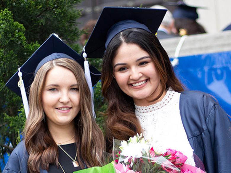 两个面带微笑的女孩，戴着毕业帽，穿着毕业服